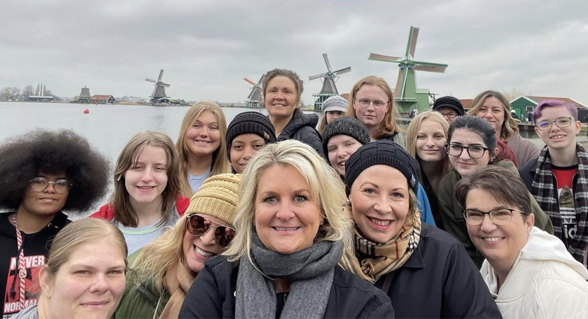 A group of teachers and students smiling in front of windmills. 