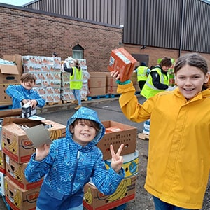 Volunteers in high-visibility vests and casual clothing sort and pack food boxes outside a warehouse on a cloudy day.