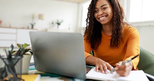 Image of a young female Connections Academy student in a yellow sweater looking at her laptop making a list about her future plans. 